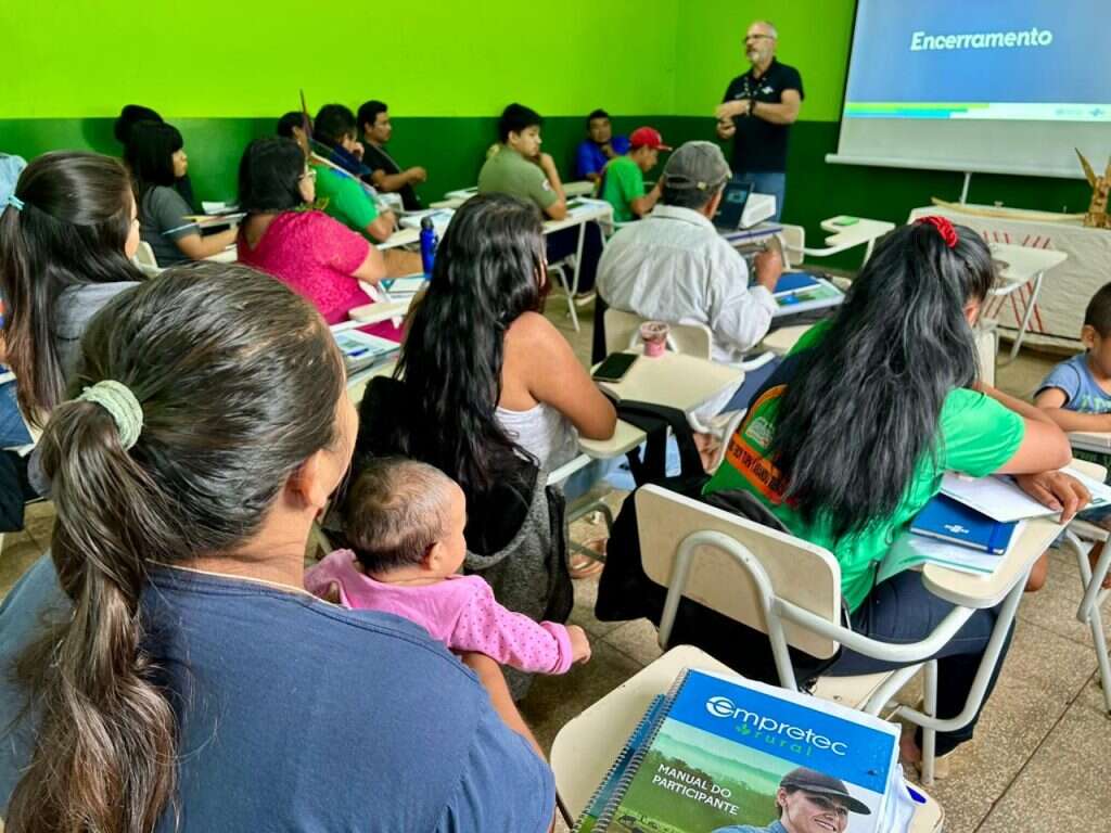 Imagem de uma sala de aula cheia durante o evento de encerramento do Empretec. Vários participantes estão sentados em carteiras, prestando atenção a um instrutor barbudo, que está em pé e apresenta a tela de projeção com a palavra "Encerramento". Uma mulher na frente segura um bebê.